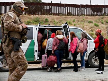 SAN DIEGO, CALIFORNIA - MAY 13: Customs and Border Protection officers walk as immigrants enter a vehicle to be transported from a makeshift camp between border walls, between the U.S. and Mexico, on May 13, 2023 in San Diego, California. Some of the immigrants at the open air camp have …