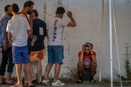 Survivors of the June shipwreck off the coast of Greece stand outside a warehouse at the port in Kalamata town
